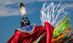 Native American in Colorful Traditional Attire and Headdress Against Blue Skies
