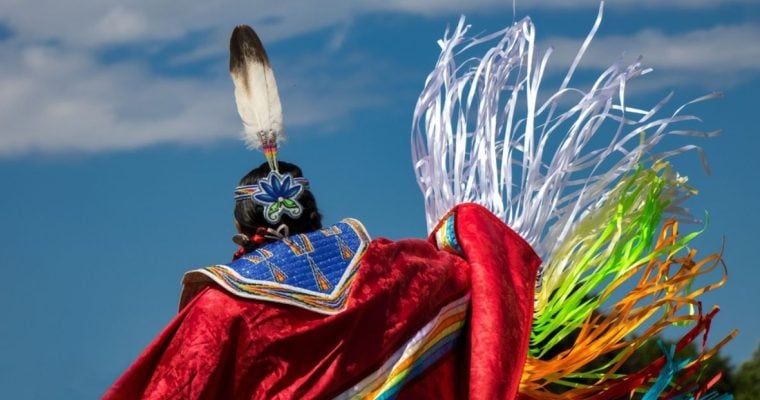 Native American in Colorful Traditional Attire and Headdress Against Blue Skies