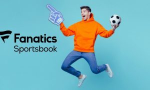 Man Wearing Jeans and Orange Hoodie Holds Soccer Ball While Jumping Next To Fanatics Sportsbook Logo