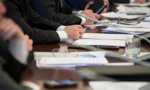 Members Of A Committee Sit At A Desk With Documents For a Hearing