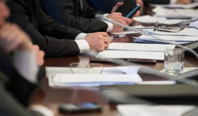 Members Of A Committee Sit At A Desk With Documents For a Hearing