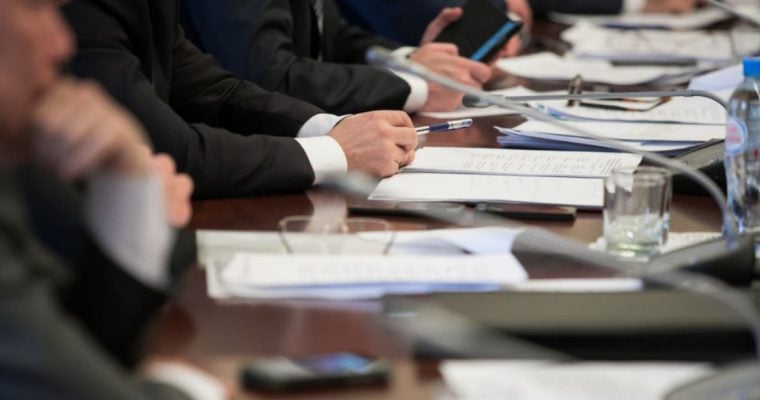 Members Of A Committee Sit At A Desk With Documents For a Hearing