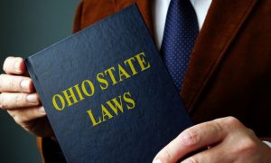 Man in Brown Suit Jacket Holds Blue Book With Ohio State Laws on Cover