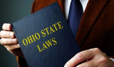 Man in Brown Suit Jacket Holds Blue Book With Ohio State Laws on Cover