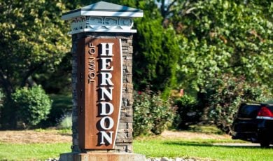 Green Trees Surround Outside Sign That Says Town of Herndon