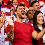 American Soccer Fans Cheer While Watching a Game Dressed in Red, White and Blue Clothes and Sporting Flags
