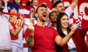 American Soccer Fans Cheer While Watching a Game Dressed in Red, White and Blue Clothes and Sporting Flags