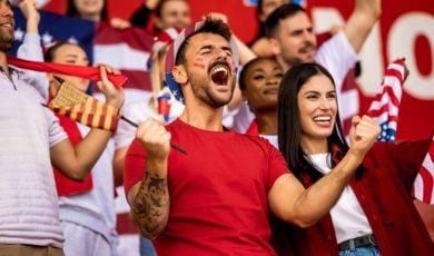 American Soccer Fans Cheer While Watching a Game Dressed in Red, White and Blue Clothes and Sporting Flags