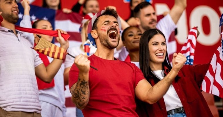 American Soccer Fans Cheer While Watching a Game Dressed in Red, White and Blue Clothes and Sporting Flags