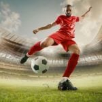 Soccer Player in Red Uniform Kicks Soccer Ball on Green Grass Field