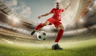Soccer Player in Red Uniform Kicks Soccer Ball on Green Grass Field