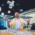 Happy Man Sits In Office In Front of Laptop Throwing Cash In the Air