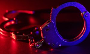 Red and Blue Lights Shine on Metal Handcuffs Sitting on Table