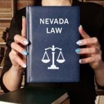 Woman Holds Blue Book With Nevada Law Text and Scale on Cover While Standing In Library