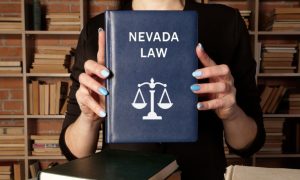 Woman Holds Blue Book With Nevada Law Text and Scale on Cover While Standing In Library