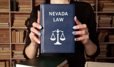 Woman Holds Blue Book With Nevada Law Text and Scale on Cover While Standing In Library