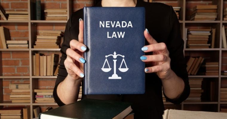 Woman Holds Blue Book With Nevada Law Text and Scale on Cover While Standing In Library
