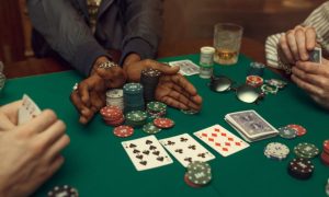 Three Poker Players Sit At Green Game Table with Chips, Playing Cards and Cash on It