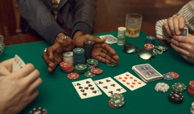 Three Poker Players Sit At Green Game Table with Chips, Playing Cards and Cash on It