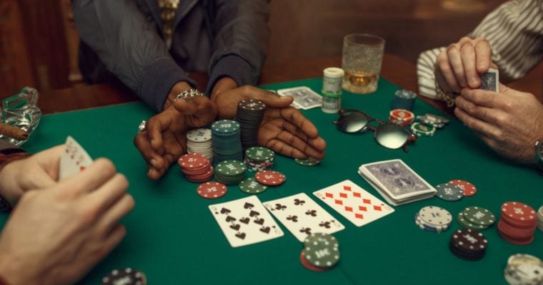 Three Poker Players Sit At Green Game Table with Chips, Playing Cards and Cash on It