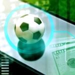 Soccer Ball Sits On Top of Mobile Phone with $100 Bills Cash Sitting at Bottom Right Corner