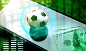 Soccer Ball Sits On Top of Mobile Phone with $100 Bills Cash Sitting at Bottom Right Corner