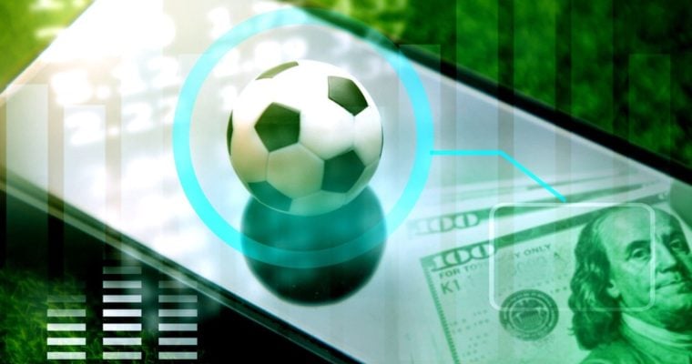 Soccer Ball Sits On Top of Mobile Phone with $100 Bills Cash Sitting at Bottom Right Corner
