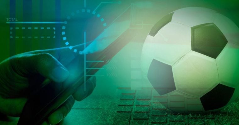 Soccer Ball Sits on Compute Keyboard with Man Holding Cell Phone in Online Sports Betting Concept