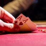 Man Plays Poker Reveals Two Aces on Red Gaming Table With Chips