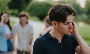 Man with Anxiety and Social Problem Excludes Himself From Friend Group in Background