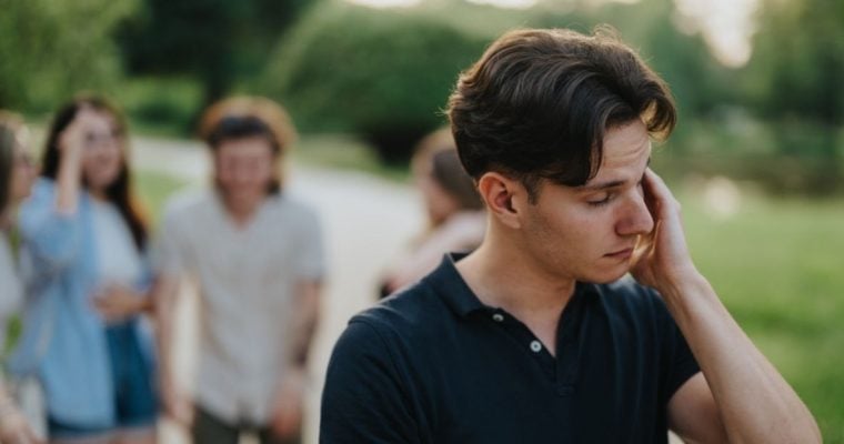 Man with Anxiety and Social Problem Excludes Himself From Friend Group in Background