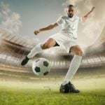 Soccer Player in White Uniform Kicks Ball in Grassy Stadium Field