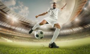 Soccer Player in White Uniform Kicks Ball in Grassy Stadium Field