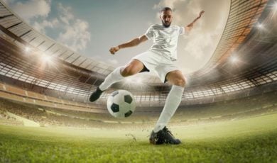 Soccer Player in White Uniform Kicks Ball in Grassy Stadium Field