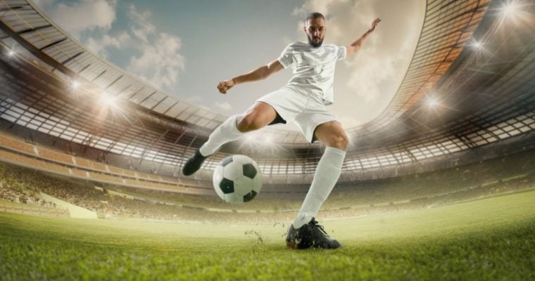Soccer Player in White Uniform Kicks Ball in Grassy Stadium Field