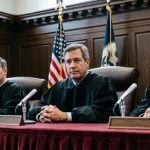 Three Judges Sit Inside Courtroom with Wooden Walls