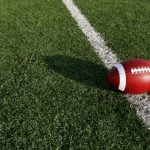 Sun Casts a Shadow of Football on Grassy American Football Field