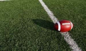 Sun Casts a Shadow of Football on Grassy American Football Field
