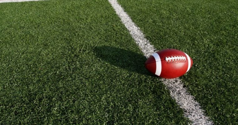 Sun Casts a Shadow of Football on Grassy American Football Field