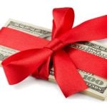 Red Ribbon Wraps a Stack of American $100 Banknotes on White Background