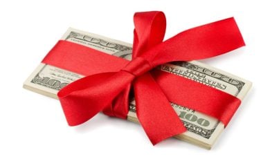 Red Ribbon Wraps a Stack of American $100 Banknotes on White Background