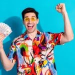Man with Yellow Glasses and Colorful Shirt Hold Fanned Cash with Happy Expression