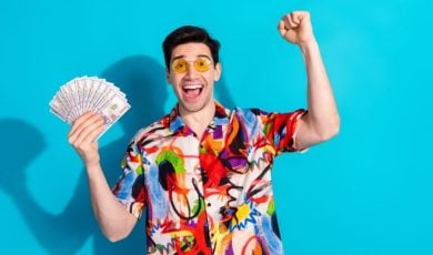 Man with Yellow Glasses and Colorful Shirt Hold Fanned Cash with Happy Expression
