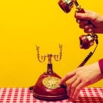 Man in Suit Picks Up Headset of Vintage Corded Telephone on Checkered Table
