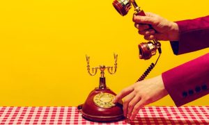 Man in Suit Picks Up Headset of Vintage Corded Telephone on Checkered Table