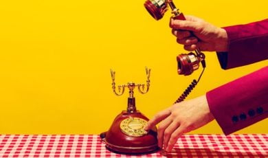 Man in Suit Picks Up Headset of Vintage Corded Telephone on Checkered Table