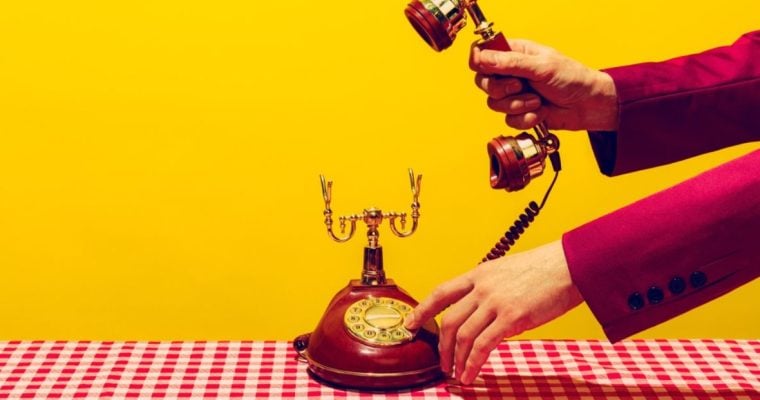 Man in Suit Picks Up Headset of Vintage Corded Telephone on Checkered Table