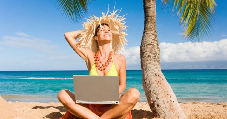 Smiling Woman Sits on Sand At Beach Under Palm Tree with Laptop