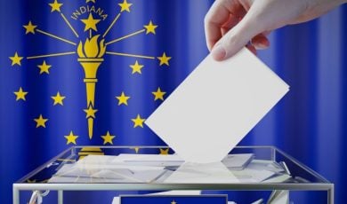 Hand Drops White Envelope Into Clear Box with Indiana State Flag Background