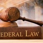 Federal Law Written on the Side of Book Sitting on Desk with Judge's Gavel and Courthouse Background
